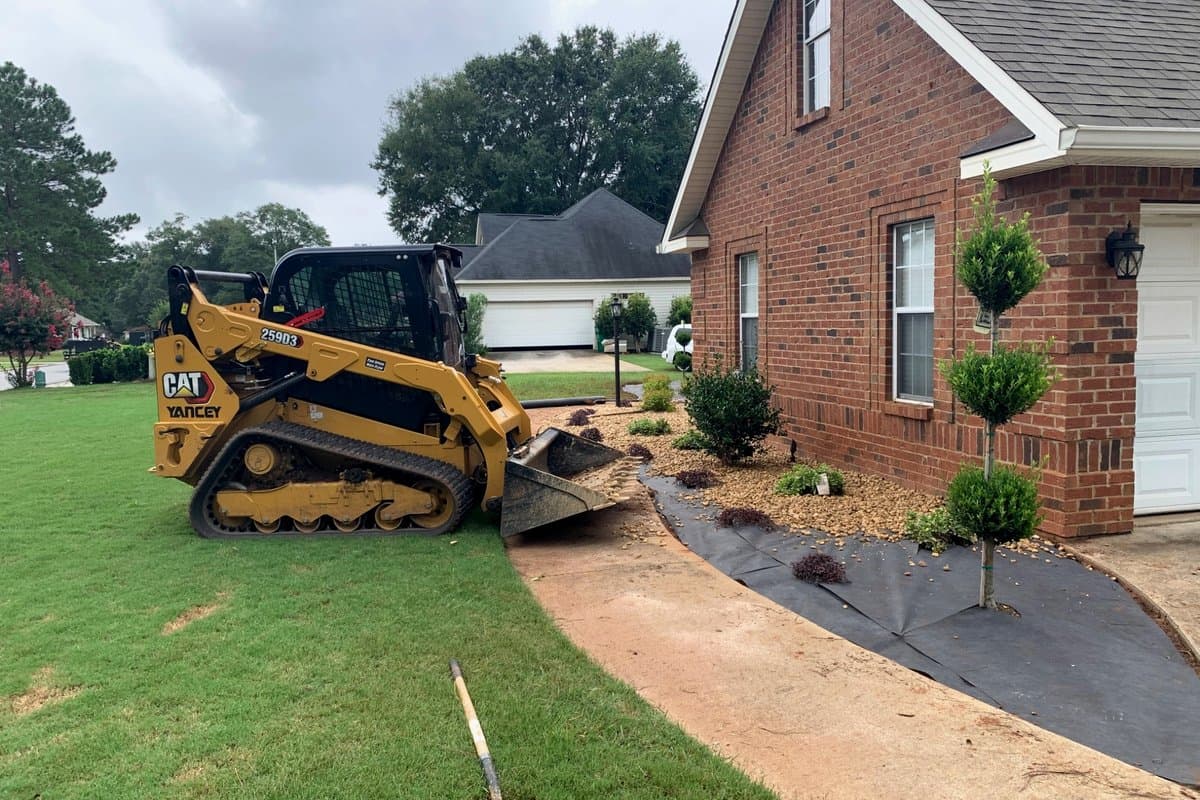 Arrowhead crew equipment shaping new beds along the side of the same brick home during installation
