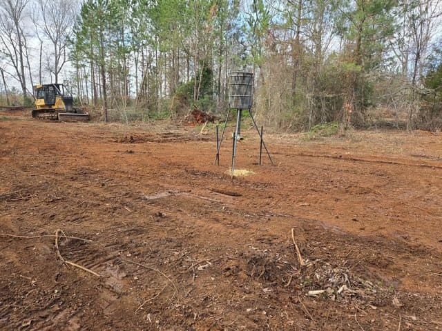A dozer and a newly set feeder on freshly cleared red clay ground at the edge of the woods